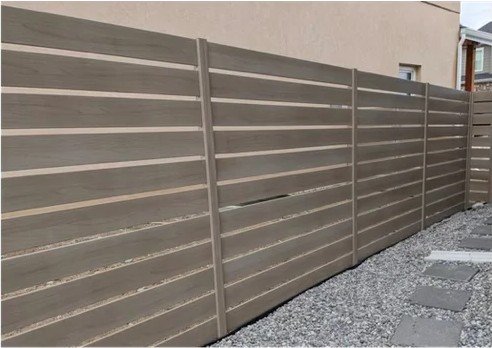 Horizontal aluminum slat fence in a driftwood finish along a side yard walkway